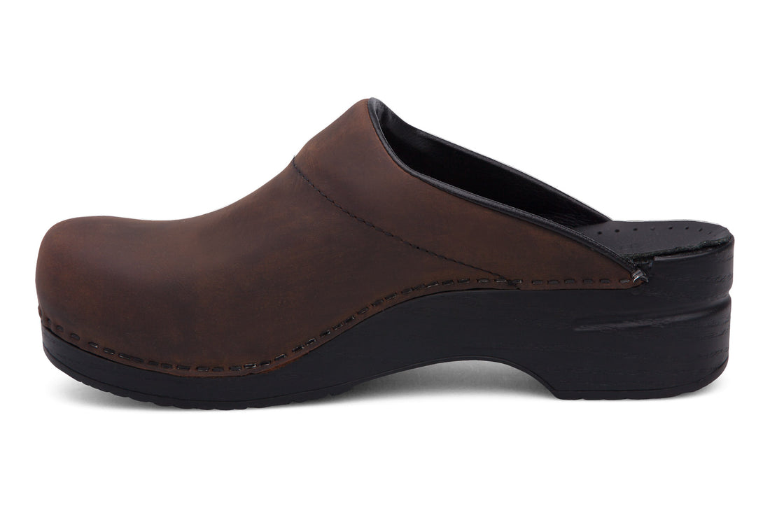 Clog, brown leather, closed toe, open heel; Dansko Karl mens with plantar fasciitis support and black sole, side view.