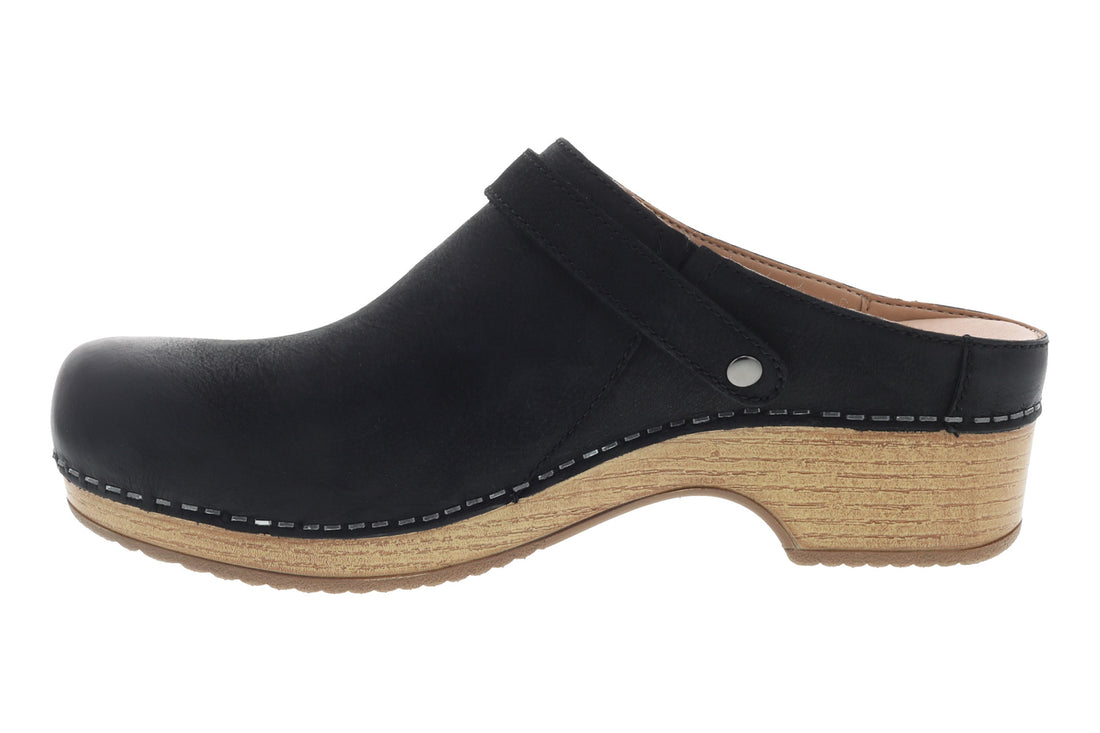 Mule shoe, black leather, Dansko Berry with side buckle, wooden sole, white stitching. Comfort features not visible.